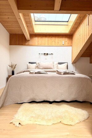 Ein Schlafzimmer mit Dachfenster, einem Bett mit Quilzdecke, einem flauschigen Teppich und Holzwänden.