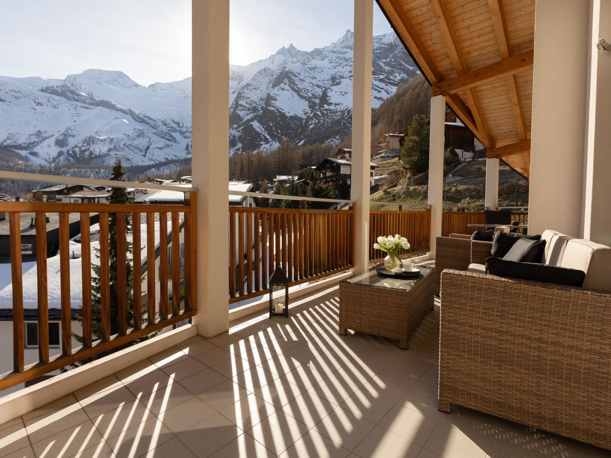 Un balcone con vista su montagne innevate, ringhiere in legno e un divano in vimini con cuscini.