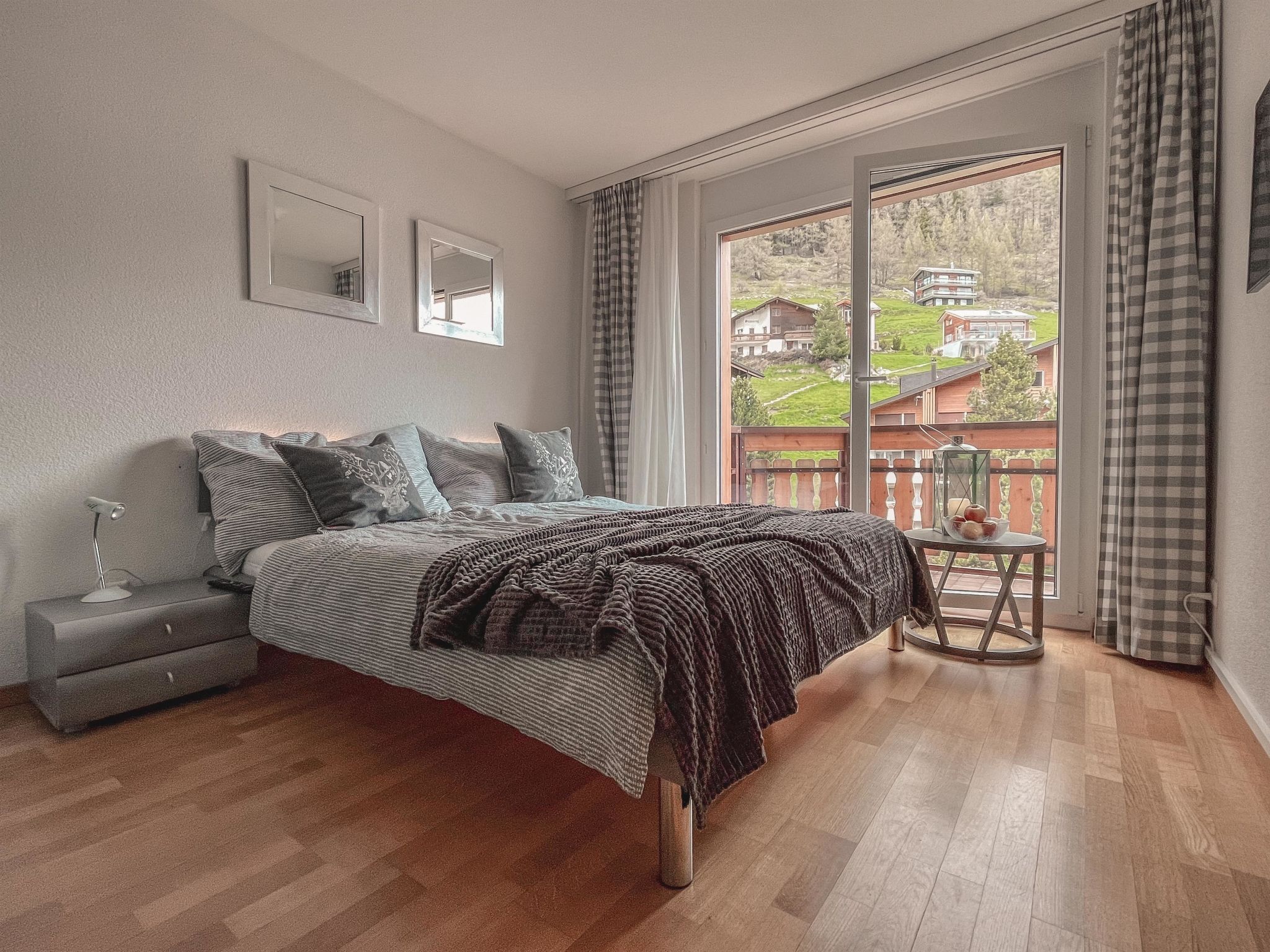 Una camera da letto con un letto grande, un comodino, una lampada, una finestra vista case e un balcone con tavolo e sedie.