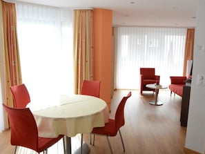 Un comedor con una mesa redonda y sillas rojas, una mesita con una silla roja, y un sofá con un cojín rojo al fondo.