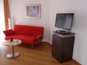 A room with a red sofa, a small round table with a red candle, a television on a wooden stand, and a framed picture on the wall. - Feehof Appartement/Fewo 2-Bettwohnung Nr. 1 by Interhome (Saas-Fee)