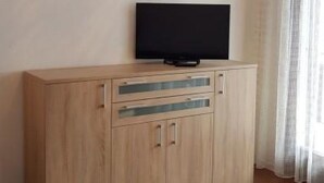 Um quarto com um armário de madeira, uma televisão de tela plana em cima e uma janela com cortinas.