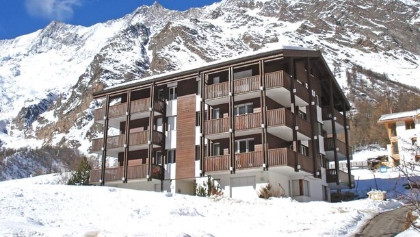 Hotel de vários andares com varandas, com montanhas nevadas ao fundo.