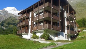 Um edifício com vários andares e varandas, com montanhas ao fundo.
