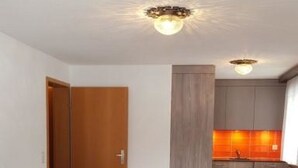 Uma sala de estar com um sofá azul, uma porta de madeira e uma área de cozinha com mesa e cadeiras.
