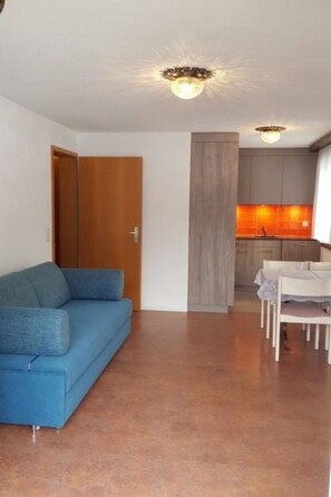 Ein Wohnzimmer mit blauem Sofa, einer Holztür und einer Küchenzeile mit Esstisch und Stühlen.