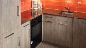 Uma cozinha moderna com armários de madeira, lava-louças preta e painel de fundo vermelho.