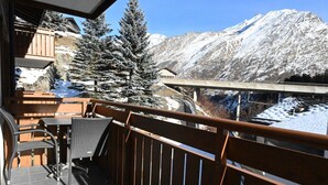 En balkon med udsigt til sneklædte bjerge, et trægelænder og et bord med stole.