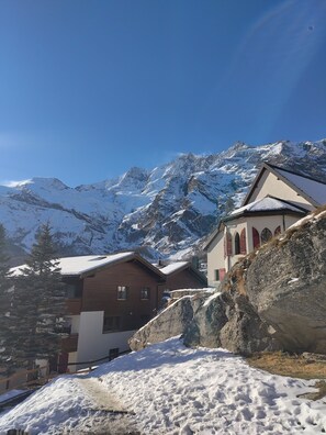 Eine Berglodge mit schneebedeckten Dächern, Holzhütten und Blick auf verschneite Berge.