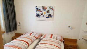 Een kamer met twee eenpersoonsbedden, een schilderij aan de muur, een nachtkastje en een klein dressoir.