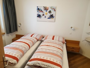 A twin room with two beds, a painting on the wall, a bedside table, and a small drawer unit. - Achat Appartement/Fewo 4-Bettwohnung Nr. 3 by Interhome (Saas-Fee)