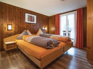 A wooden-paneled bedroom with a bed, bedside tables, and a large window with curtains. - Chalet Alpenruh Appartement/Fewo Nr. 4 Allalin by Interhome (Saas-Fee)