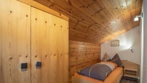 Una habitación de madera con una cama, un armario y un techo inclinado.