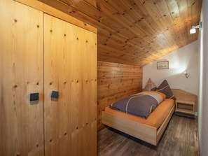 A wooden room with a bed, a wardrobe, and a sloped ceiling. - Chalet Alpenruh Appartement/Fewo Nr. 4 Allalin by Interhome (Saas-Fee)