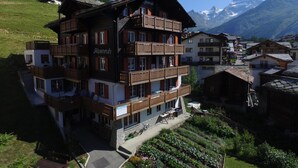 Un hotel de varios pisos con balcones, un jardín y montañas al fondo.