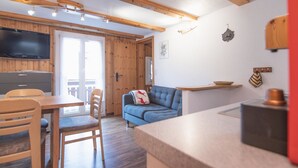 Una cocina moderna con vigas de madera, un comedor con sillas, un sofá y un televisor montado en la pared.