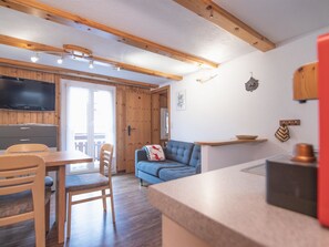 A modern kitchen with wooden beams, a dining area with chairs, a sofa, and a television mounted on the wall. - Chalet Alpenruh Appartement/Fewo Nr. 4 Allalin by Interhome (Saas-Fee)