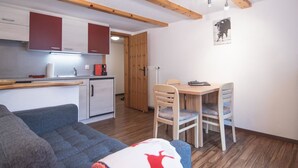 Un espacio habitable compacto con kitchenette, comedor y zona de estar con sofá y sillas.