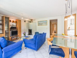 Ein modernes Wohnzimmer mit einem Glastisch, blauen Sofas, einem Flachbildfernseher und einem Kamin.