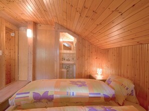 Ein Zimmer in einer Holzhütte mit einem Bett, einem Nachttisch und einem durch eine Tür sichtbaren Badezimmer.