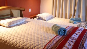 A hotel room with two beds, a headboard, a wall-mounted light, and a window with curtains.