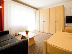 A hotel room with a sofa, a small table with a plant, a wooden wardrobe, and a television on the wall. - Aiglon Appartement/Fewo 2-Bettwohnung Nr. 2 by Interhome (Saas-Fee)