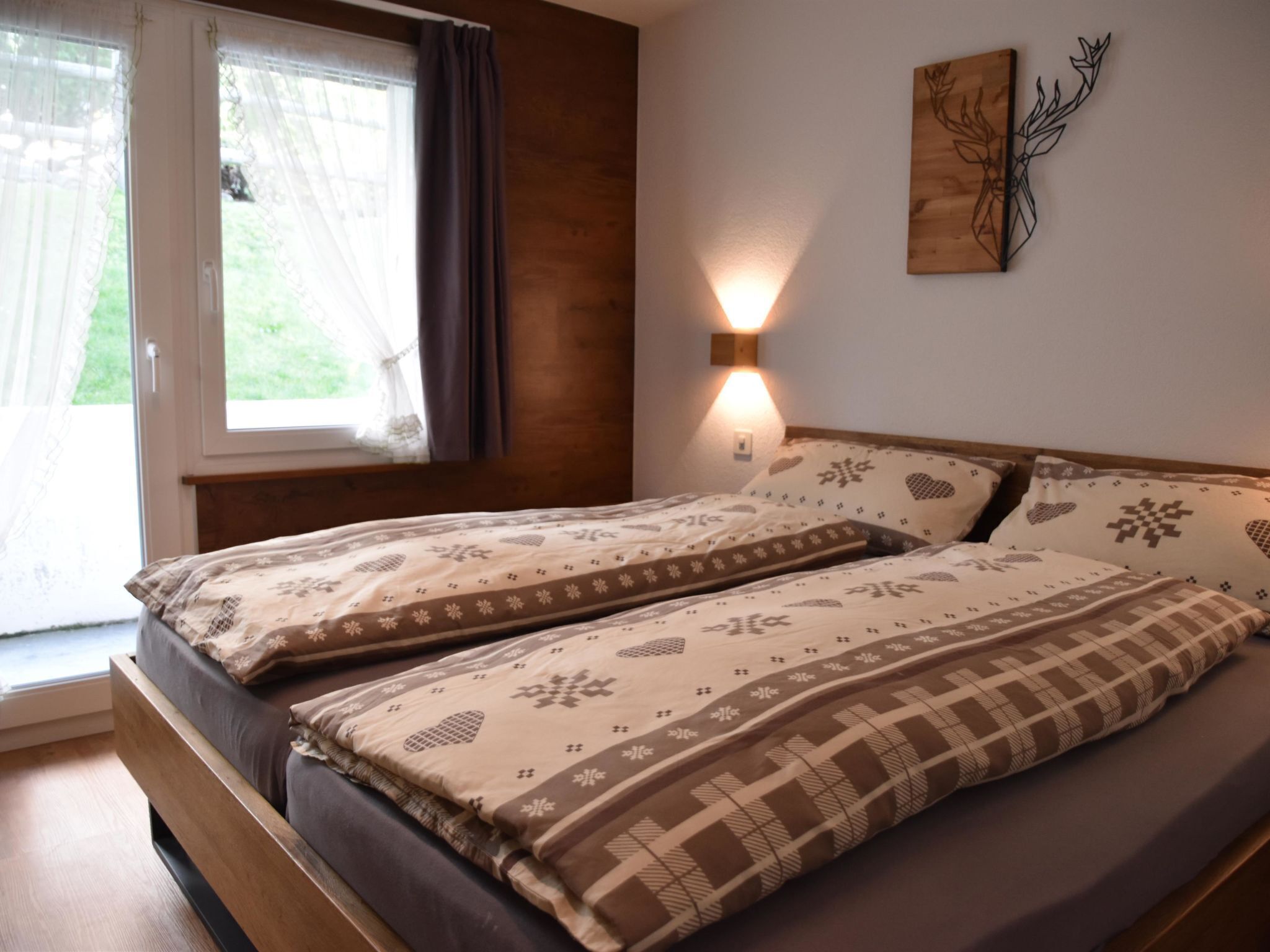 Ein Doppelbett mit gemusterten Betttextilien, ein Fenster mit Vorhängen, eine Wandleuchte und ein dekoratives Element über dem Bett.