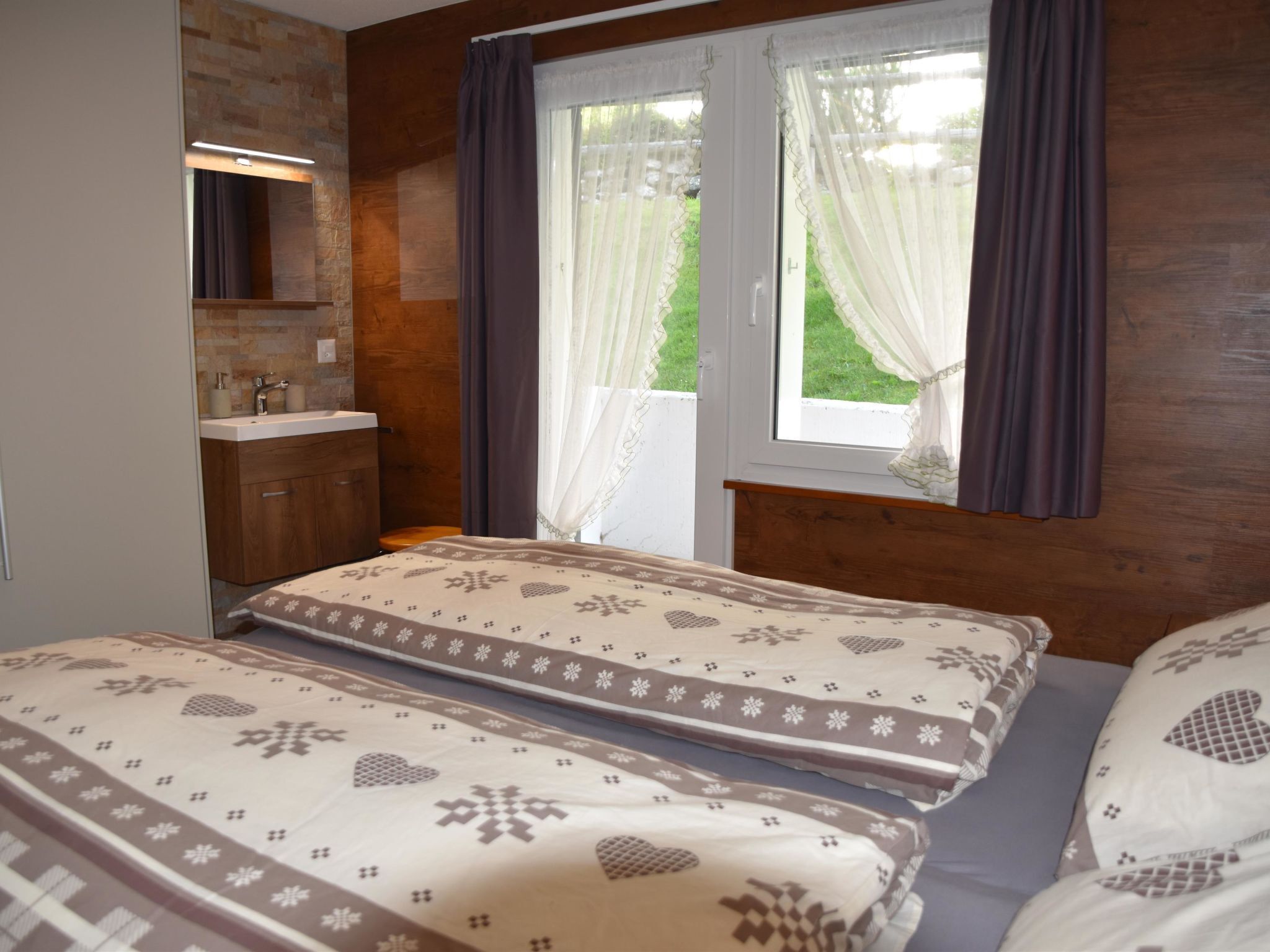 A bedroom with two beds, a bathroom, and a window with curtains.
