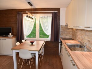 Een moderne keuken met een houten tafel, stoelen, een inbouwoven en een raam met gordijnen.