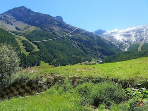 Eine gebirgige Landschaft mit blauem Himmel, einer Hängebrücke und einer Steinmauer.