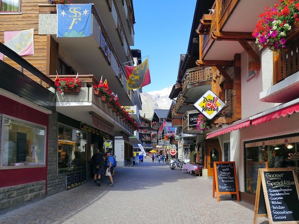 A narrow street with shops and balconies adorned with flowers, a sign for 'Donat Metzger', and a chalkboard menu. - Amedee Appartement/Fewo 5-Bettwohnung Nr. 1 by Interhome (Saas-Fee)