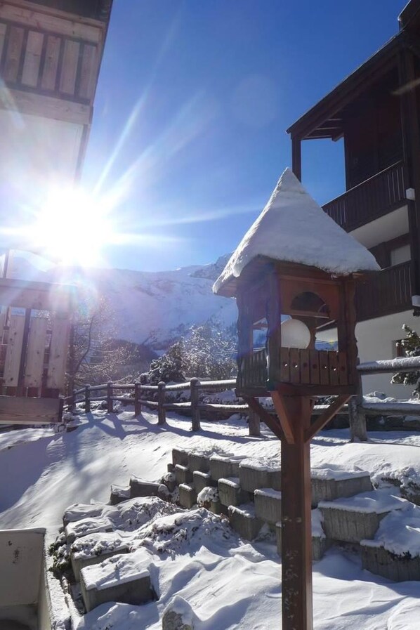 Ein Vogelhaus aus Holz mit einem mit Schnee bedeckten Dach, vor dem Hintergrund eines strahlend blauen Himmels und eines schneebedeckten Berges.
