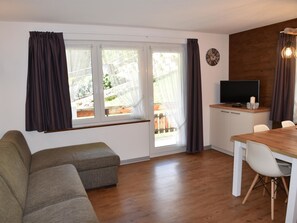 A living room with a sofa, a dining table with chairs, a television, and a clock on the wall. - Amedee Appartement/Fewo 5-Bettwohnung Nr. 1 by Interhome (Saas-Fee)