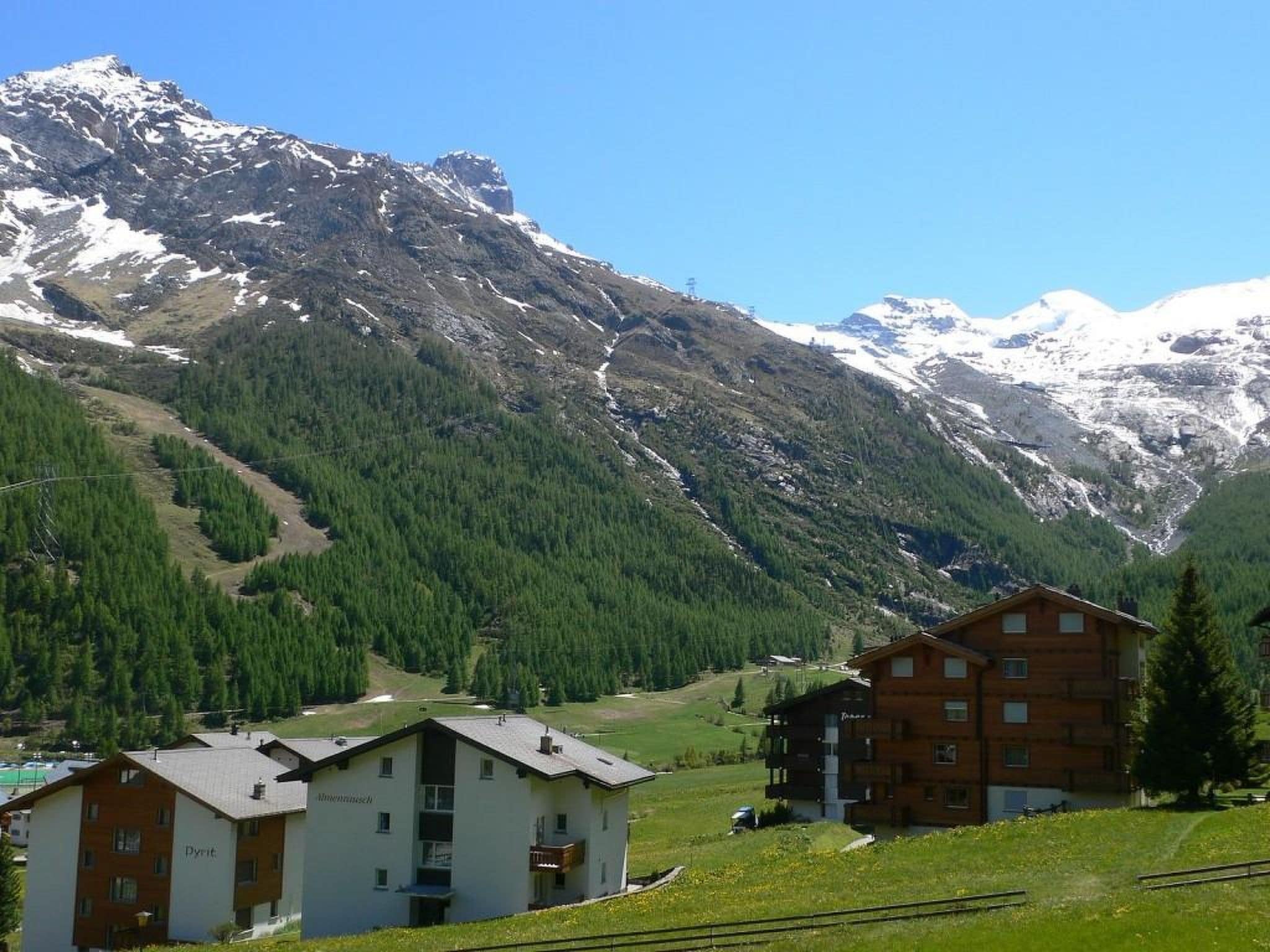 A mountain landscape with a chalet-style building featuring multiple balconies and a ski slope in the background.