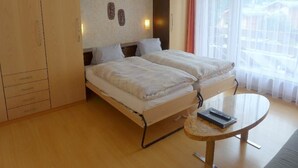 Ett hotellrum med två sängar, ett litet runt bord och utsikt över omgivningen genom tunna, genomskinliga gardiner.
