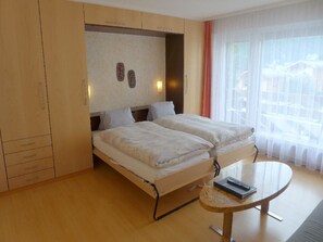 A hotel room with two beds, a small round table, and a view of the outside through sheer curtains. - Acimo Appartement/Fewo 2-Bettwohnung Muschi by Interhome (Saas-Fee)