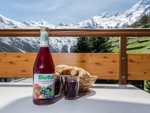 Eine Flasche Biotta Superfrüchte, ein Korb mit Brot und zwei Gläser Saft auf einem Tisch mit Blick auf die Berge.