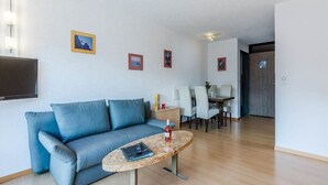 Ett vardagsrum med en blå soffa, ett soffbord, en tv som är monterad på väggen och en matplats med stolar och ett bord.