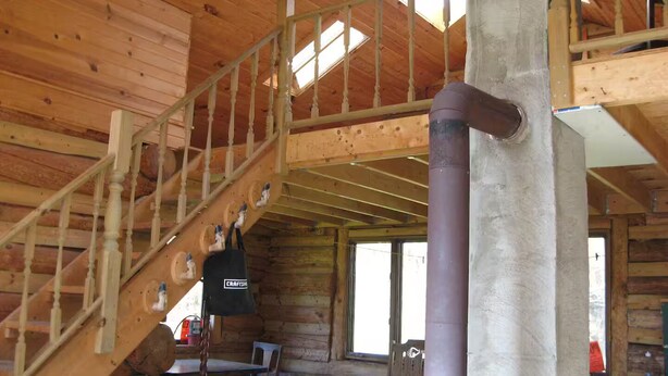 Interior d'una cabana de fusta amb escala, taula de dinar i finestra gran.