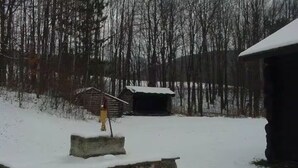 A snow-covered outdoor area with a stone platform, a wooden structure, and a building with a snow-covered roof.