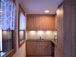 A kitchen with wooden cabinets, a sink, and a window with a curtain. - Topas Appartement/Fewo 4-Bettwohnung Nr. 13 by Interhome (Saas-Fee)