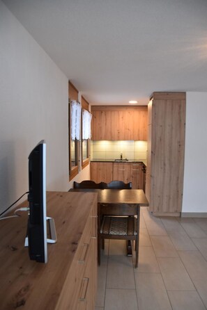 A compact kitchen with wooden cabinets, a dining table, and a television. - Topas Appartement/Fewo 4-Bettwohnung Nr. 13 by Interhome (Saas-Fee)
