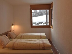A bedroom with two beds, a window with a view of a snowy landscape, and a wall-mounted light. - Topas Appartement/Fewo 4-Bettwohnung Nr. 13 by Interhome (Saas-Fee)