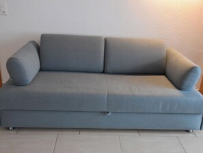 Um sofá cinzento com uma almofada em cada extremidade, apoiado contra uma parede lisa.