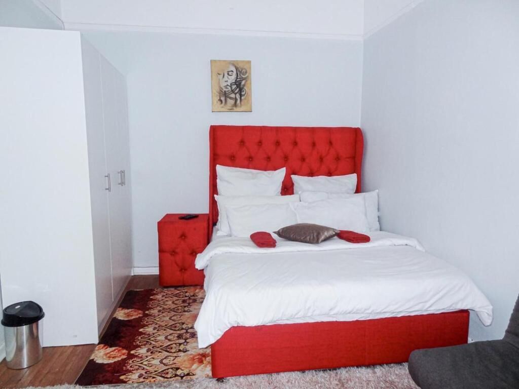 Un dormitorio con cabecera roja, ropa de cama blanca y alfombra estampada.