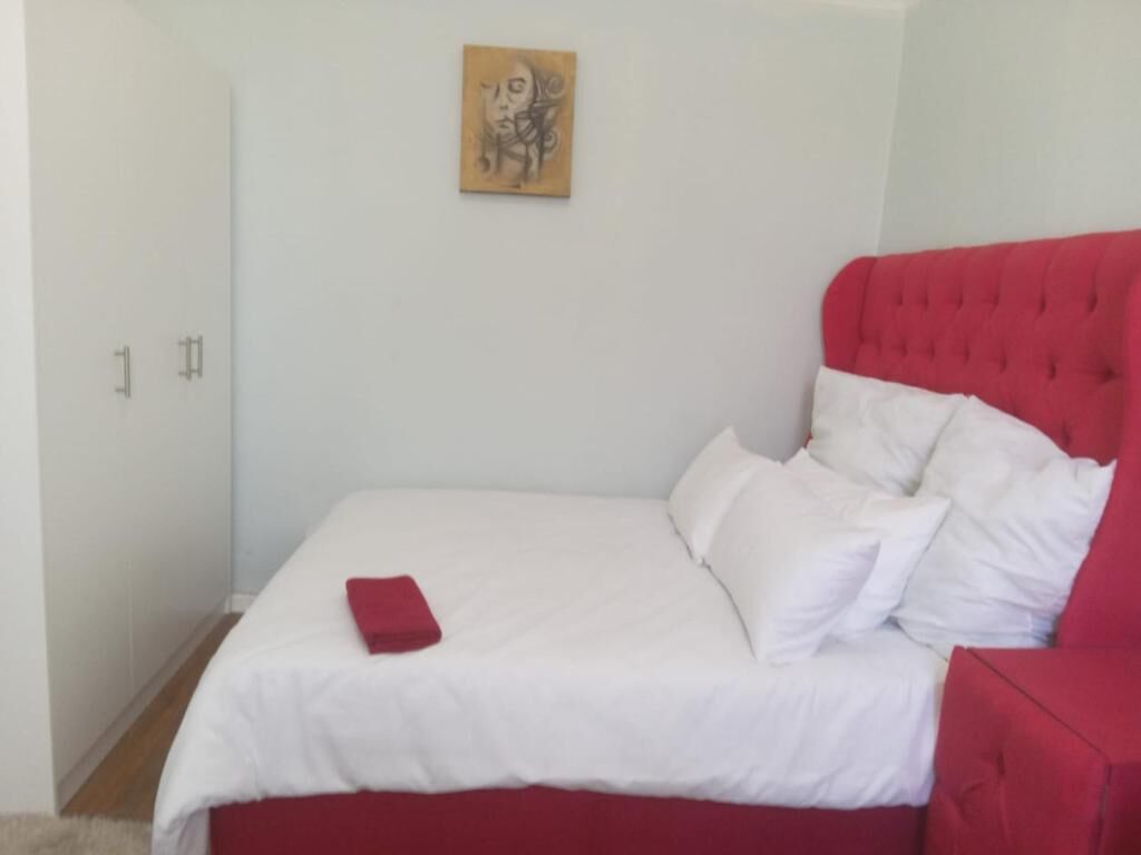 A bedroom with a bed, a red headboard, white bedding, and a wall-mounted artwork.