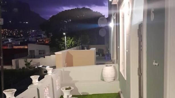 Terraza en la azotea con vistas a la ciudad al anochecer, un pequeño jardín y una barandilla blanca.