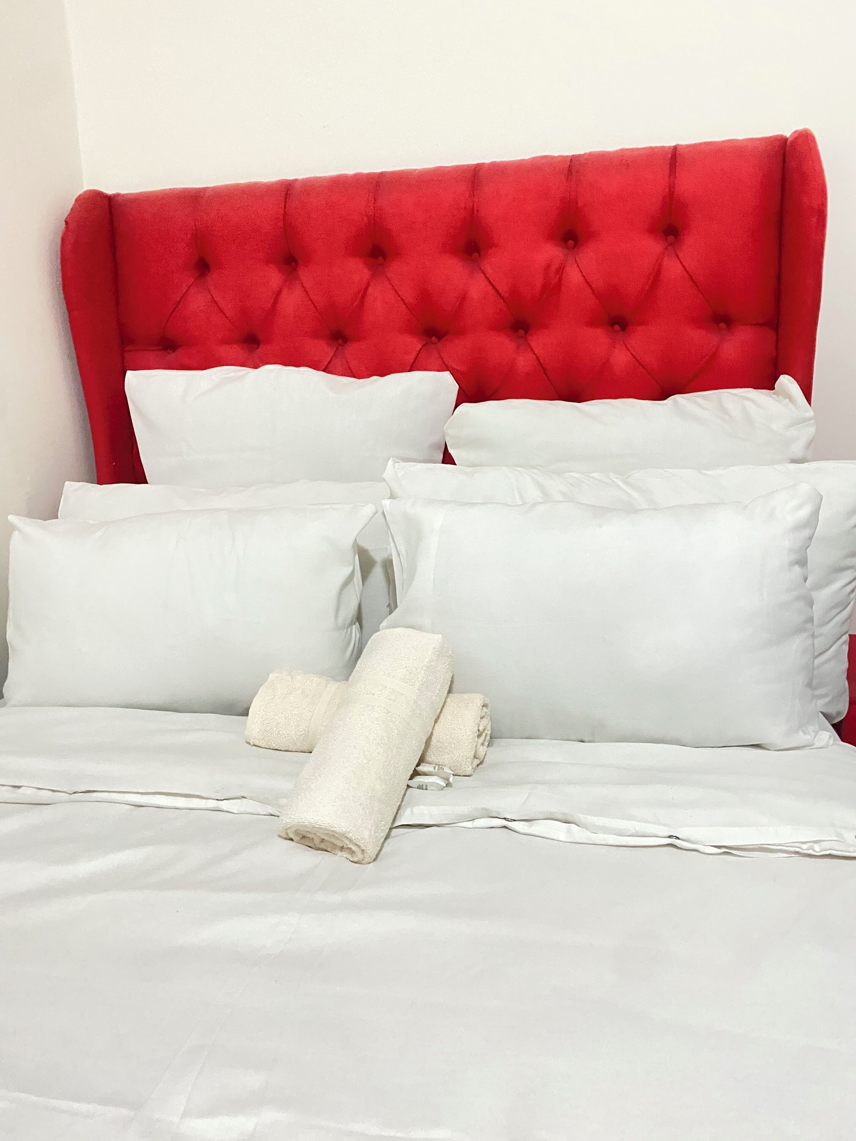 A bed with a red upholstered headboard, white pillows, and a neatly folded white towel.