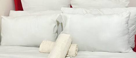 A bed with a red upholstered headboard, white pillows, and a neatly folded white towel.