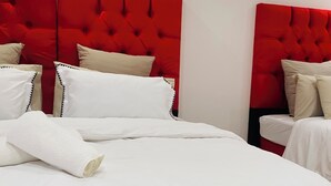 Una cama con ropa de cama blanca y cabecera roja, una almohada blanca y una toalla blanca enrollada.